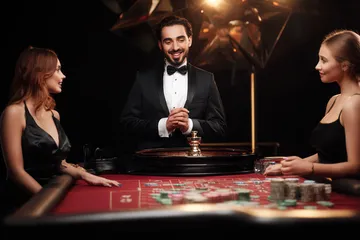 A professional dealer in a tuxedo greeting players at the roulette table, symbolizing the authentic live casino feel at OKTA.