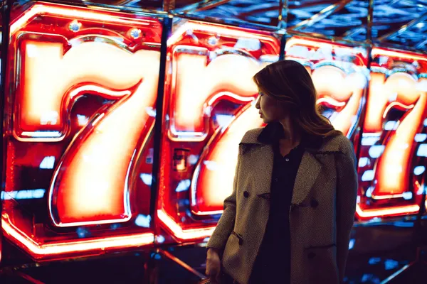 A woman smiling while playing online games on her laptop, surrounded by neon casino elements, showcasing OKTA’s diverse game collection.